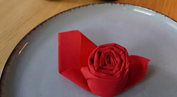 Un pliage serviette papier en forme de rose rouge sur une assiette grise. Une touche d'élégance pour une table.
