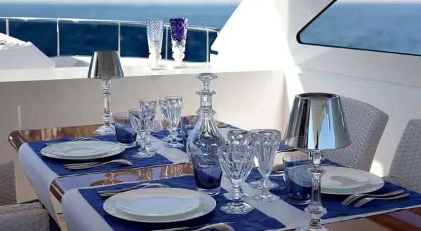 Un dîner élégant sur un yacht, avec des verres en cristal, des carafes et les différents couverts de table disposés sur des nappes bleues.