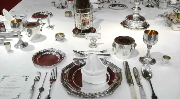 Une table dressée pour un service à l'anglaise, avec vaisselle en argent, verres, couverts et bouteille de vin.