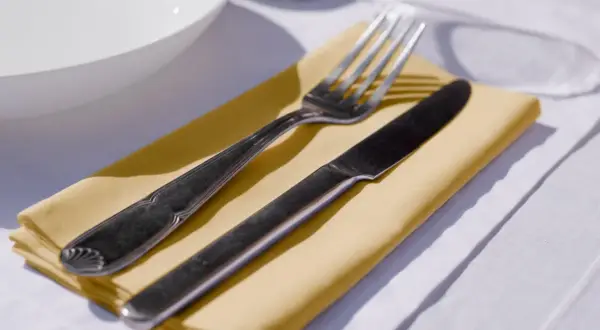 Un couteau et une fourchette reposent sur un noeud serviette de table jaune, prêt pour un repas.