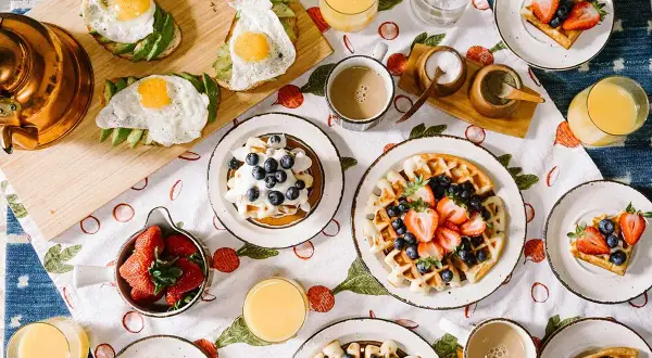 Un délicieux **heure du brunch dimanche** avec des gaufres aux fruits, des toasts à l'avocat et aux œufs, des fraises et du jus d'orange.