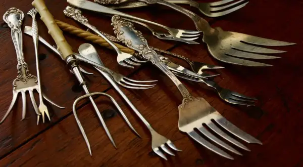 Un assortiment de fourchettes anciennes, certaines ornées, sur fond de bois. Qui a inventé la fourchette ? Ces ustensiles racontent une histoire.