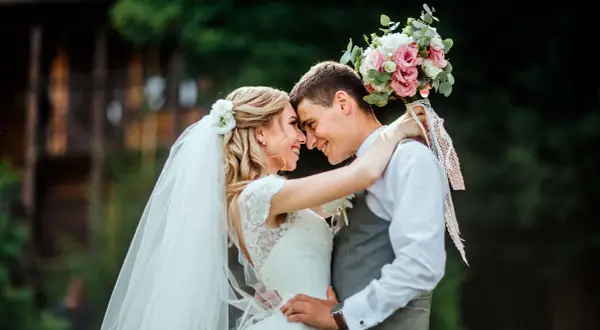 Un couple s'embrasse tendrement, le bouquet de la mariée rappelant une fête foraine. Un mariage plein de joie et d'amour.
