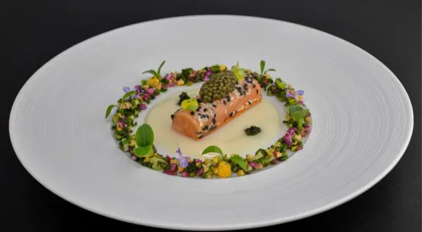 Un délicat pavé de saumon enrobé de sésame, surmonté de caviar, baignant dans une sauce onctueuse. Un plat qui pourrait faire partie d'un repas 7 services, orné de fleurs et de légumes croquants.