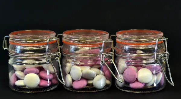 Trois bocaux en verre remplis de bonbons roses et blancs, une idée originale par quoi remplacer les dragées mariage.