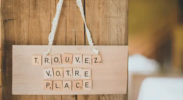 Marque place bouchon liège DIY : "Trouvez votre place" écrit avec des lettres Scrabble sur une planche en bois.