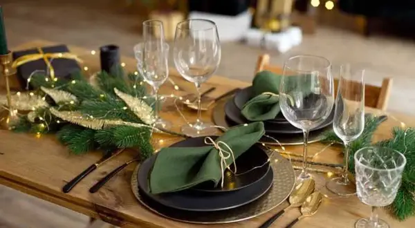 Table dressée pour Noël avec pliage serviette avec rond de serviette, guirlande lumineuse et branches de sapin.