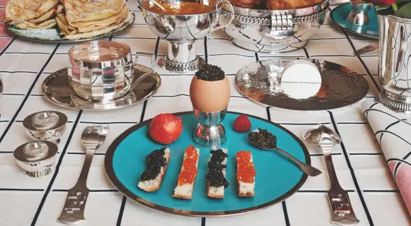 Un festin de caviar, toasts, œufs et fruits sur une table dressée avec une nappe au motif damassé.