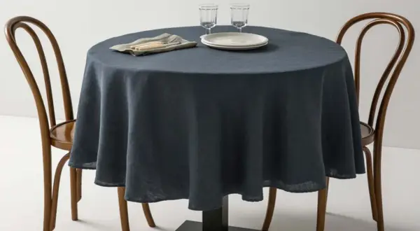 Table ronde avec nappe bleu nuit, deux chaises en bois et vaisselle. Une idée pour quel nappe choisir pour un dîner élégant.