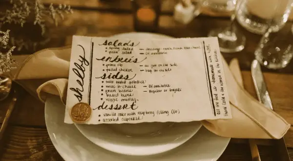 Un menu de mariage manuscrit, joliment présenté sur une assiette, détaille les entrées, accompagnements et desserts.