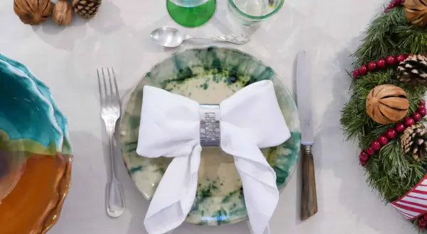 Une table dressée pour Noël avec un pliage serviette robe élégant, des pommes de pin et une guirlande festive.