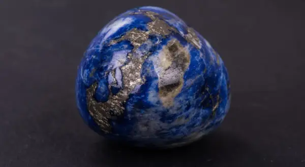 Un œuf en lapis-lazuli, rappelant les noces de saphir pour 56 ans de mariage, scintille de reflets dorés sur fond sombre.