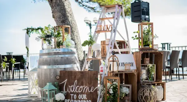 Décoration porte d'entrée pour mariage : un tonneau, une échelle décorée, des caisses en bois et des lanternes accueillent les invités.