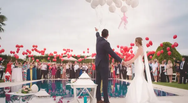 Un couple de mariés, entouré d'invités, lâche des ballons blancs et rouges. Un lâcher de ballon mariage symbolisant l'amour et l'espoir.