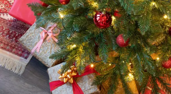 Idée tuto sapin de noël : des cadeaux emballés sous un sapin décoré de boules rouges et de guirlandes lumineuses.