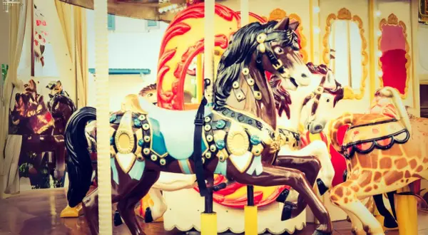 Chevaux décorés sur un manège de fête foraine, avec des touches de roses dans les ornements et les lumières.