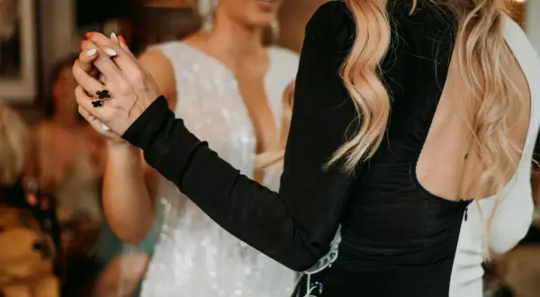 Deux femmes dansent, l'une en robe blanche scintillante, l'autre en robe noire. Elles se tiennent la main, un geste pour faire honneur au mariage.