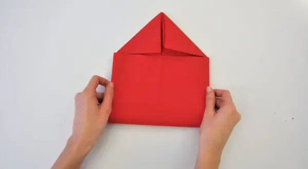 Mains tenant une feuille rouge pour un pliage serviette enveloppe. Le papier est plié en forme de maison.