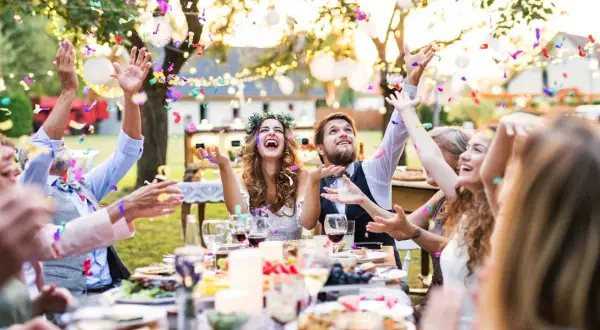 Joyeuse animation anniversaire de mariage en plein air, avec des confettis colorés pleuvant sur des invités souriants et un couple rayonnant.