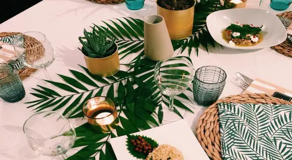 Une table dressée dans une ambiance jungle, avec des feuilles de palmier, des plantes en boîtes et des bougies.