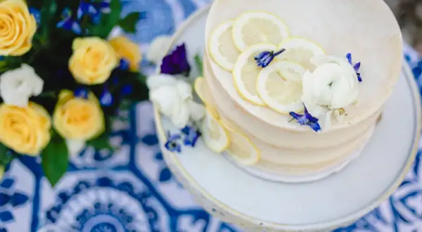 Gâteau de mariage jaune et bleu, décoré de rondelles de citron et de fleurs. Un bouquet de roses jaunes et de fleurs bleues est à proximité.