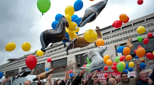 Un lâcher de ballons colorés et gonflables en forme de chevaux s'envole devant un bâtiment imposant.