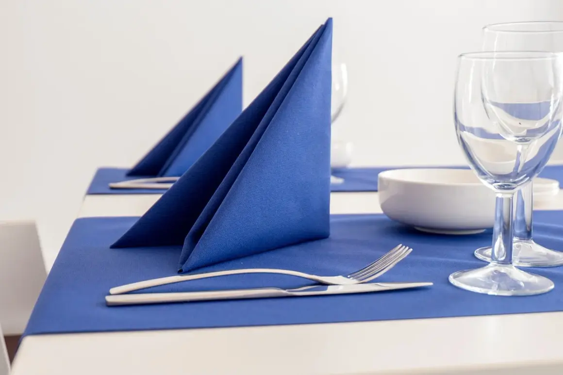 Service de table élégamment dressé avec un pliage serviette bleu vif, des couverts et des verres à vin.