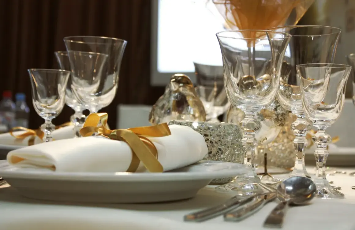 Service plat sur table avec des verres en cristal, des serviettes blanches nouées de ruban doré et des décorations scintillantes.