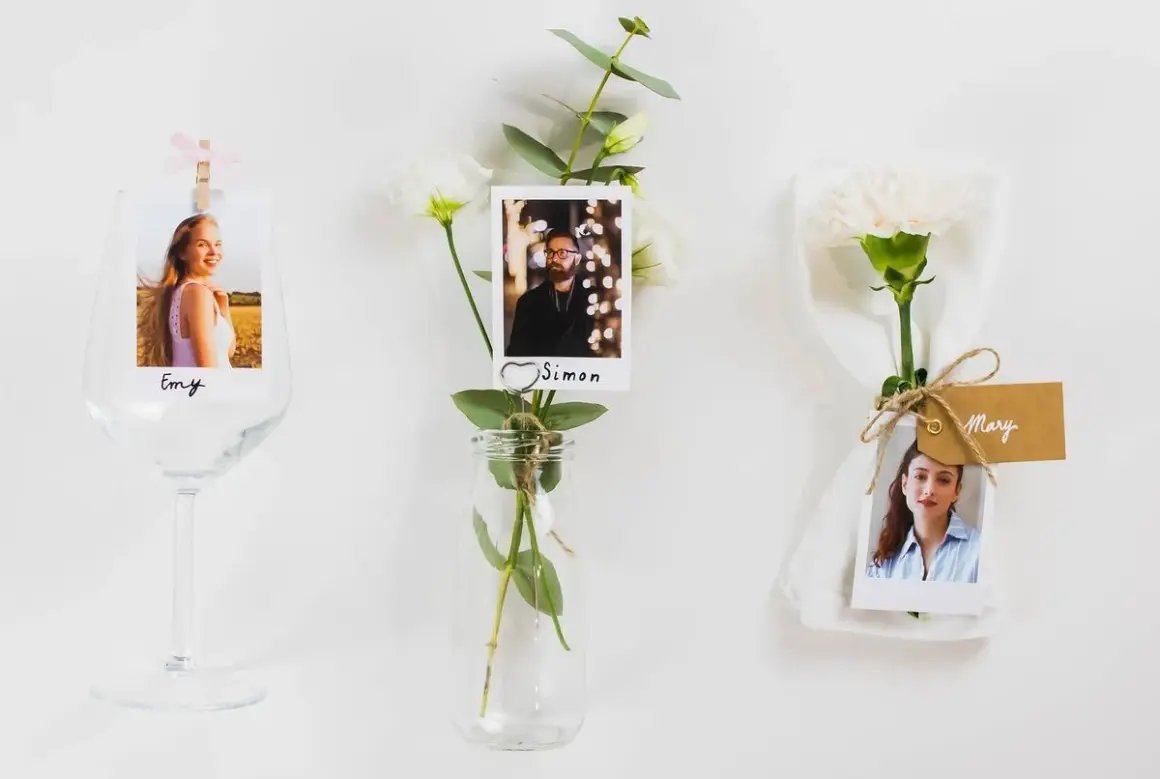 Marque place fleur : photos de invités (Emy, Simon, Mary) attachées à des fleurs et des verres, pour une décoration de table personnalisée.