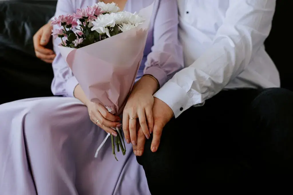 Un couple se tient la main, un bouquet de fleurs roses et blanches à la main. Un rappel doux de leur calendrier noces.