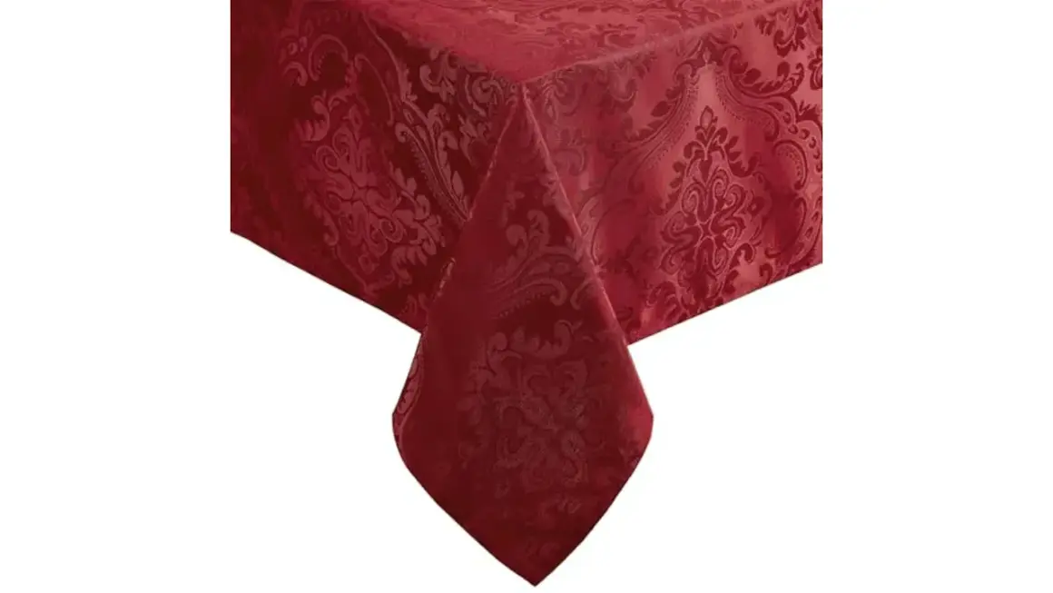 Un coin d'une table recouverte de nappes damassées rouge profond, ornées de motifs floraux complexes.
