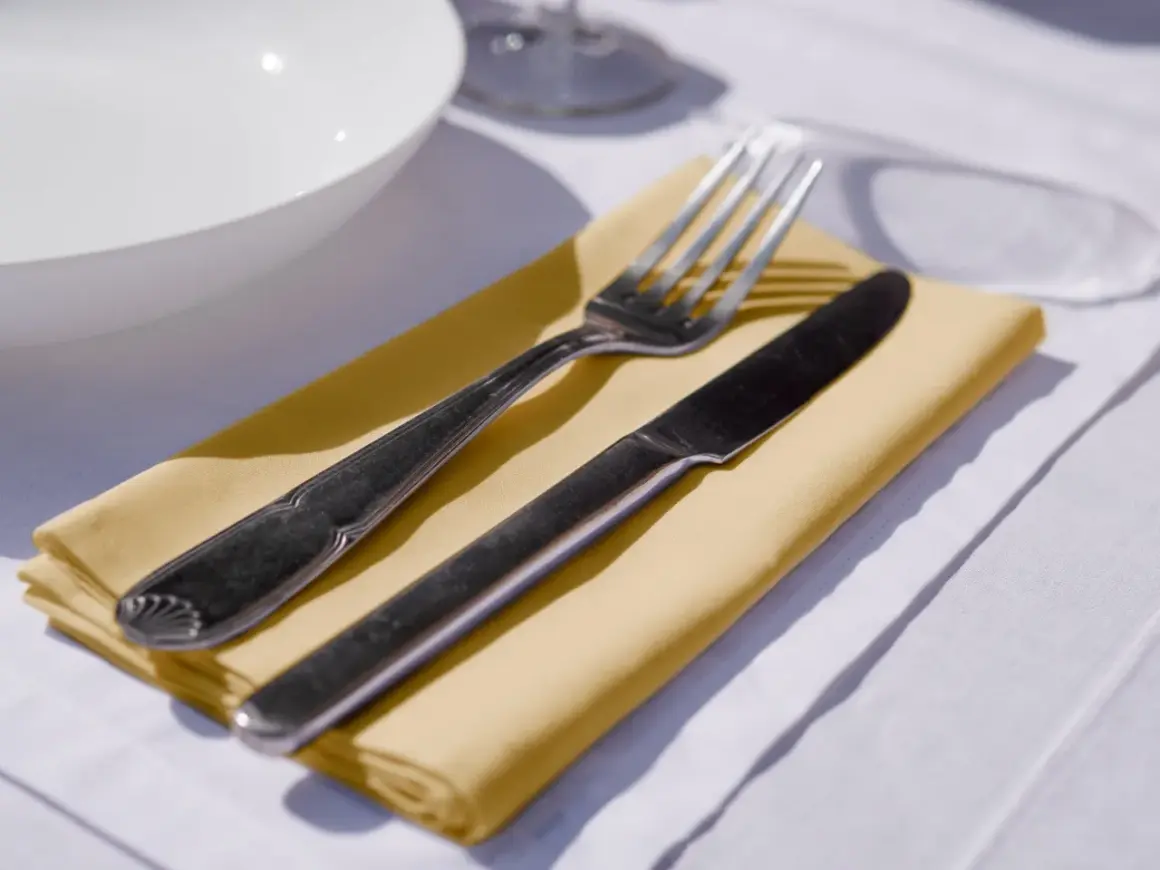 Un couteau et une fourchette reposent sur un noeud serviette de table jaune, prêt pour un repas.