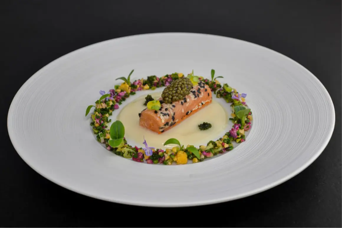 Un délicat pavé de saumon enrobé de sésame, surmonté de caviar, baignant dans une sauce onctueuse. Un plat qui pourrait faire partie d'un repas 7 services, orné de fleurs et de légumes croquants.