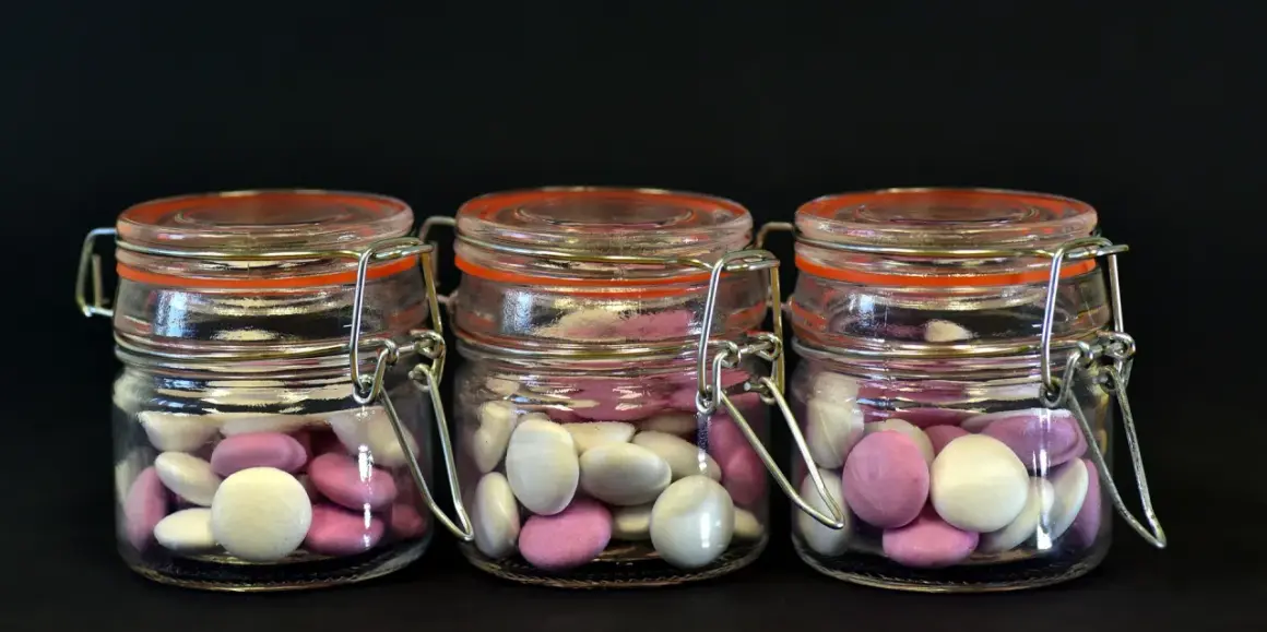 Trois bocaux en verre remplis de bonbons roses et blancs, une idée originale par quoi remplacer les dragées mariage.