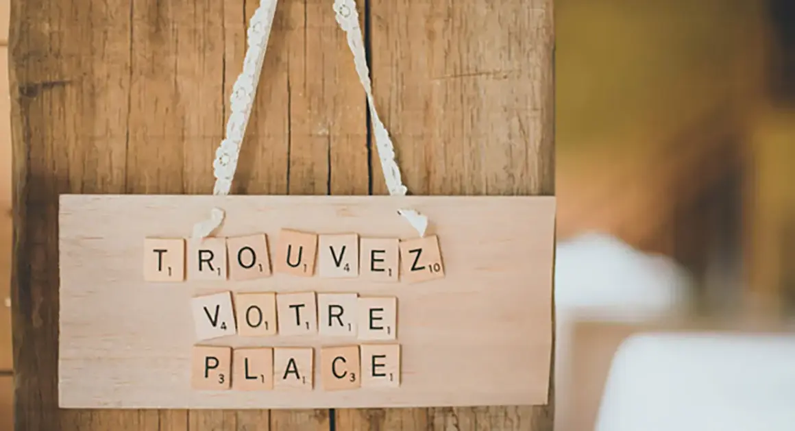 Marque place bouchon liège DIY : "Trouvez votre place" écrit avec des lettres Scrabble sur une planche en bois.