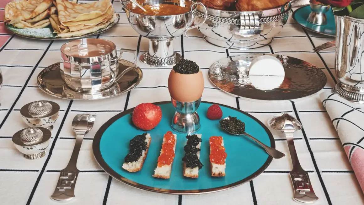 Un festin de caviar, toasts, œufs et fruits sur une table dressée avec une nappe au motif damassé.