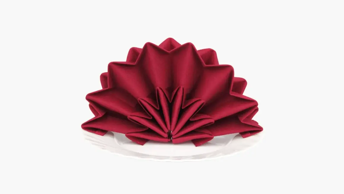 Pliage serviette tissu noël en forme d'étoile, rouge profond, sur une assiette blanche. Une touche festive pour votre table.