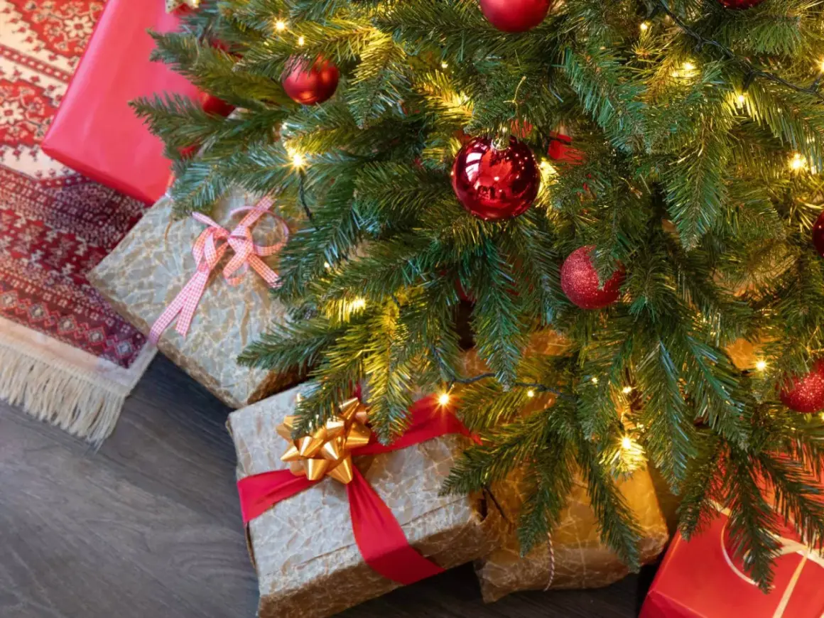 Idée tuto sapin de noël : des cadeaux emballés sous un sapin décoré de boules rouges et de guirlandes lumineuses.