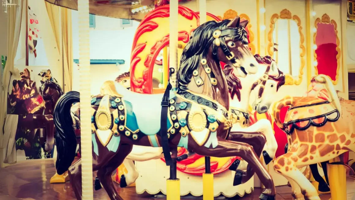 Chevaux décorés sur un manège de fête foraine, avec des touches de roses dans les ornements et les lumières.