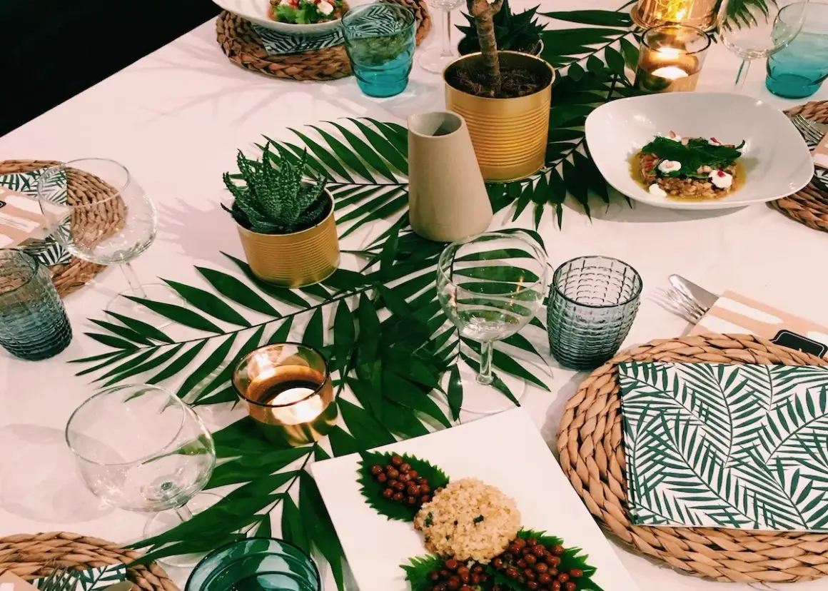 Une table dressée dans une ambiance jungle, avec des feuilles de palmier, des plantes en boîtes et des bougies.