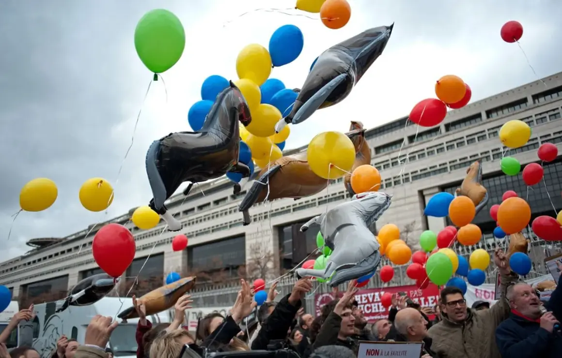 Un lâcher de ballons colorés et gonflables en forme de chevaux s'envole devant un bâtiment imposant.
