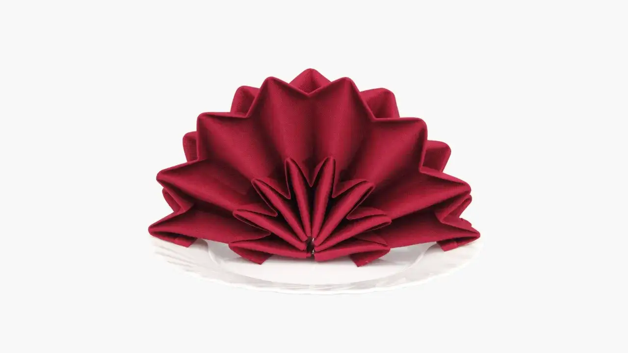 Une serviette rouge est pli&eacute;e en &eacute;ventail sur une assiette blanche. Ce pliage serviette &eacute;ventail ajoute une touche d'&eacute;l&eacute;gance.