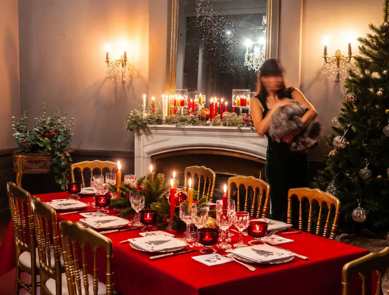 Une &eacute;l&eacute;gante deco table noel rouge et or, illumin&eacute;e par des bougies, avec une femme tenant un chat.