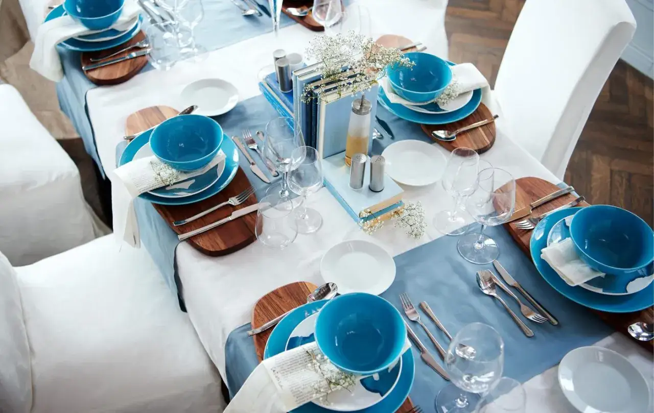 Table dressée avec des assiettes bleues, des bols et des couverts. Chaque couvert est posé sur une planche en bois, avec une fourchette à gauche.