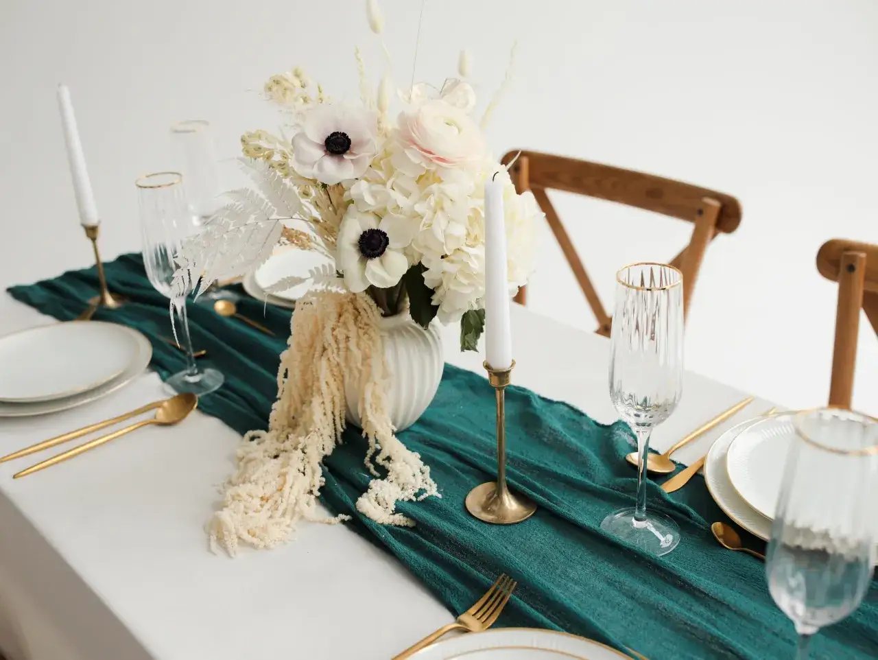 Une table dressée pour un mariage vert d'eau, avec des fleurs blanches, des bougies et de la vaisselle dorée.