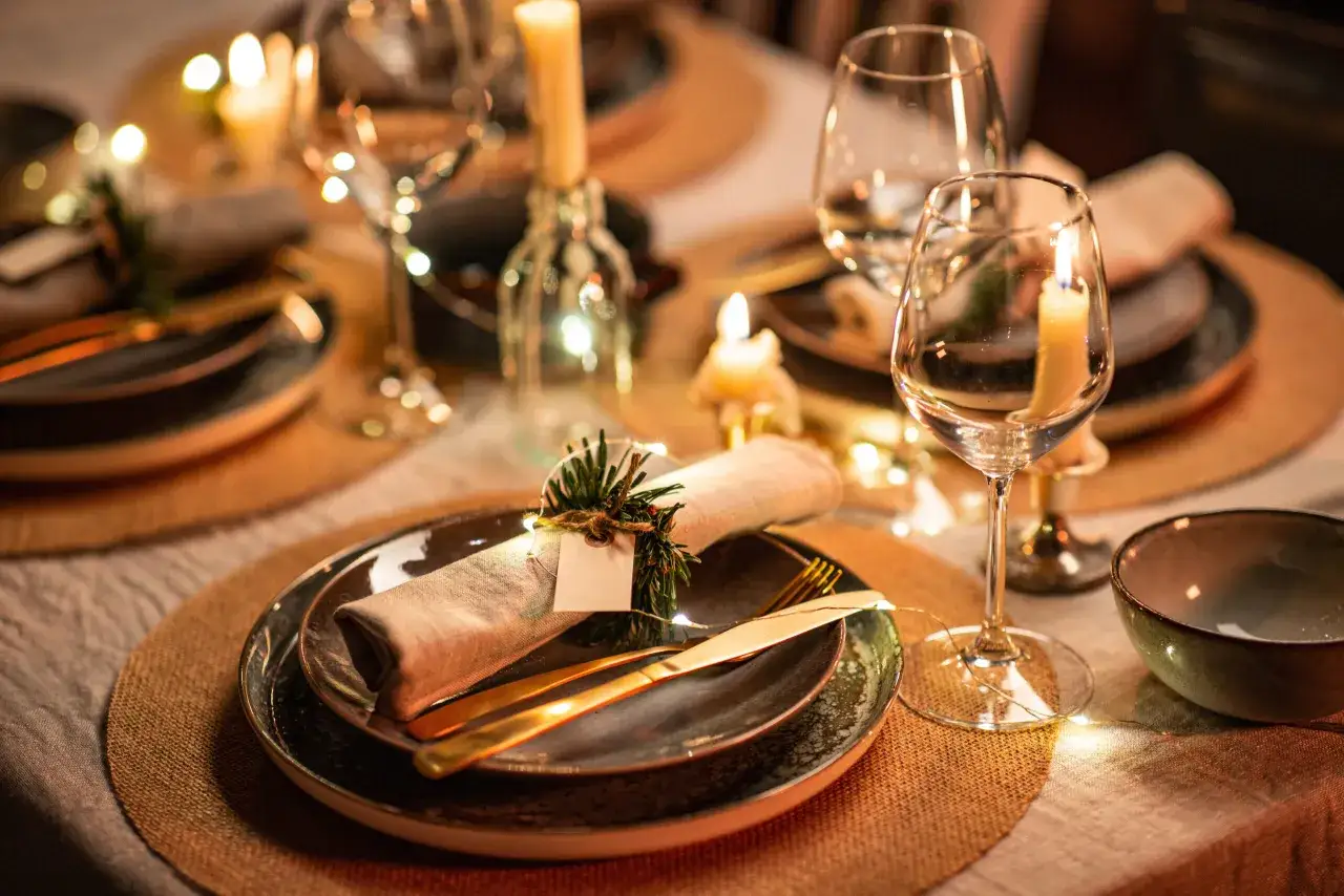 Une table dressée pour un repas festif, avec des bougies, des verres, des assiettes et un marque menu décoré de verdure.