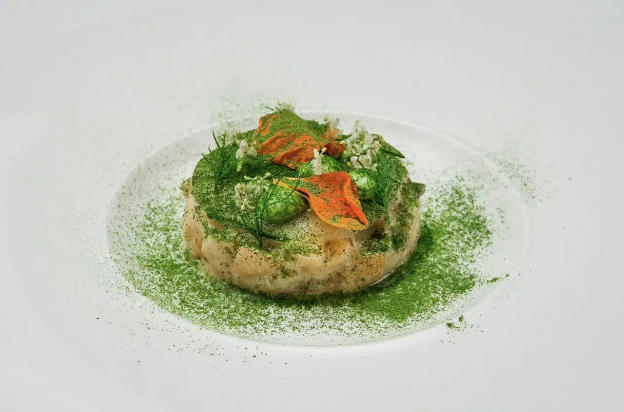 Un plat sophistiqué, un service à l'assiette d'une délicatesse exquise, orné de poudre verte et de touches orangées.