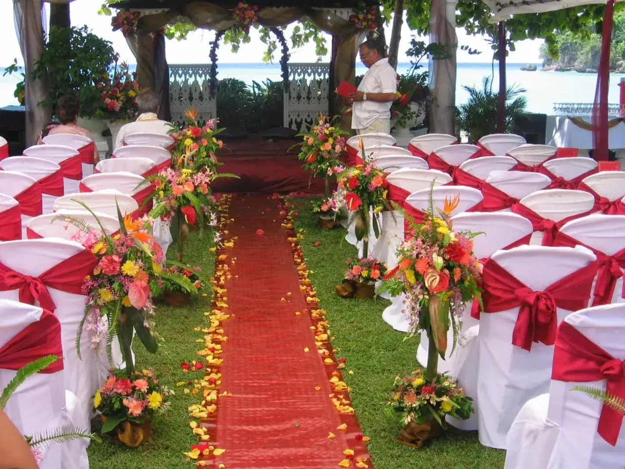 All&eacute;e de mariage th&egrave;me Japon, d&eacute;cor&eacute;e de fleurs tropicales et de p&eacute;tales de roses, avec des chaises blanches orn&eacute;es de rubans rouges.