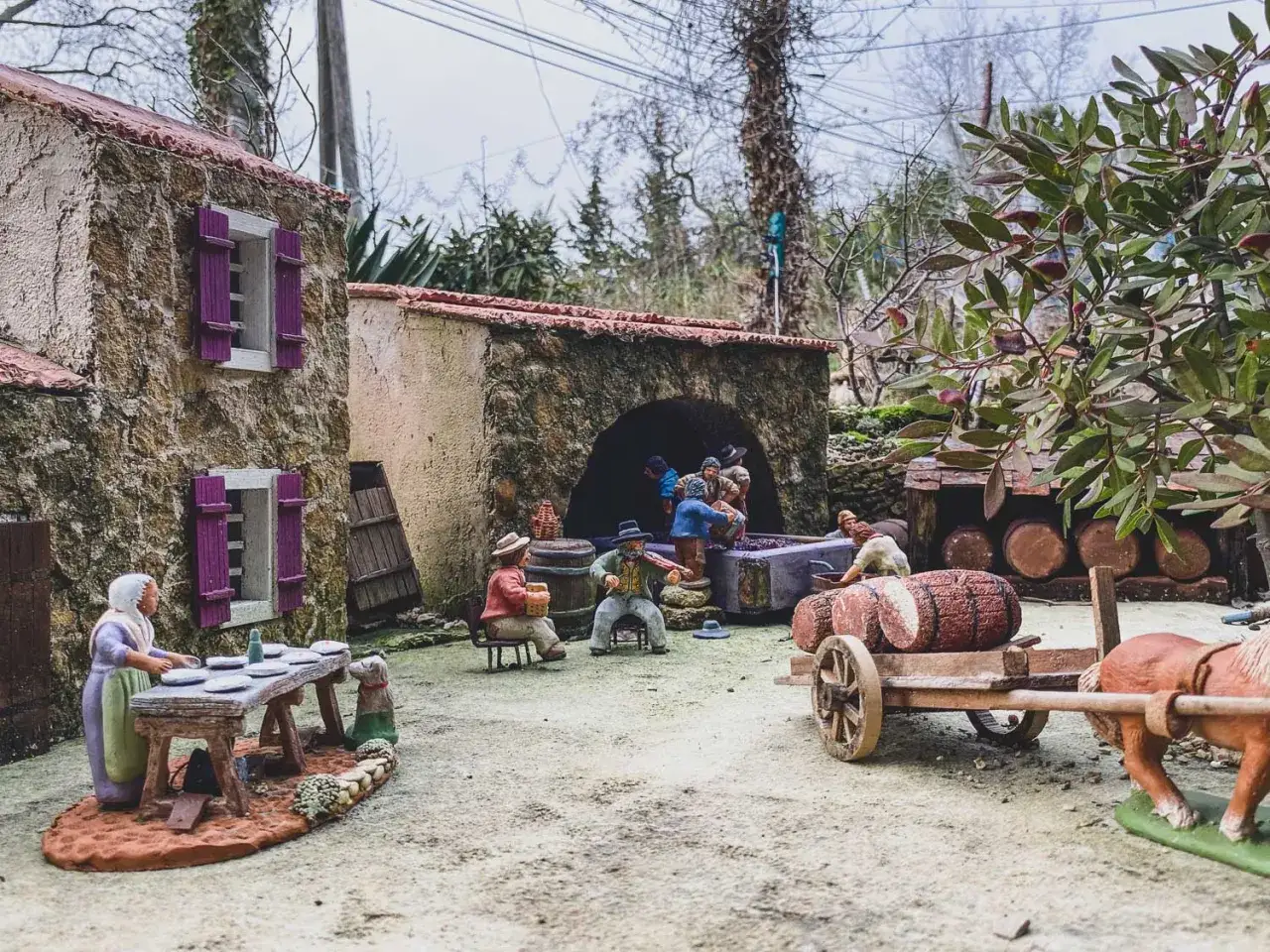 Maquette de crèche de Noël : scène de village avec personnages, maisons en pierre, tonneaux et charrette tirée par un cheval.
