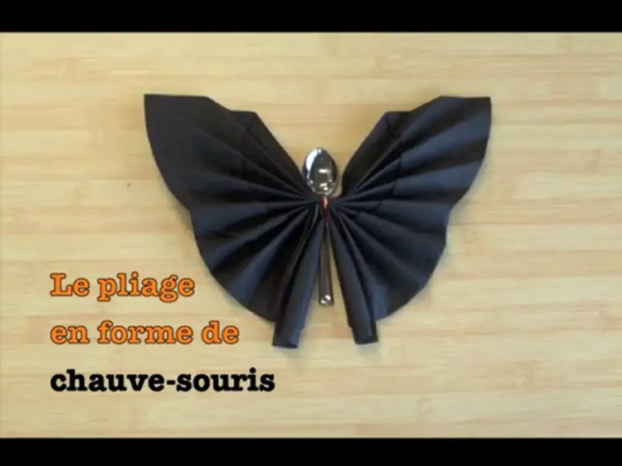 Une serviette noire pliée en forme de chauve-souris, avec une cuillère pour le corps.